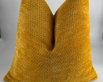 May include: A square decorative pillow in a warm mustard yellow color. The pillow has a textured, woven fabric. The pillow is a solid color and has a soft, inviting appearance. The pillow is a home decor item.