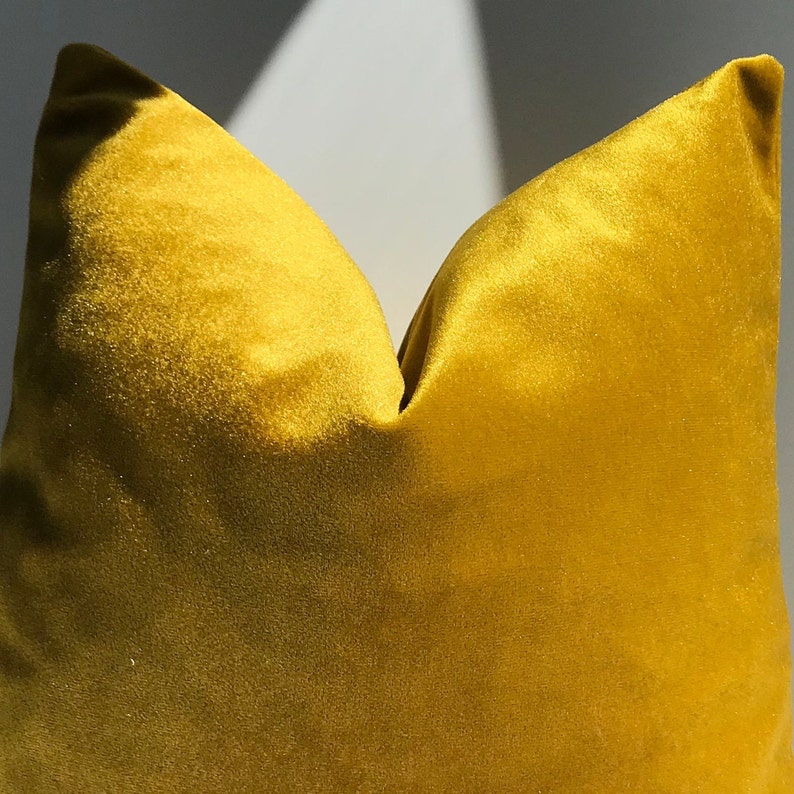 May include: A mustard yellow velvet pillow cover. The pillow cover is made of a soft, plush fabric and has a smooth, even texture.