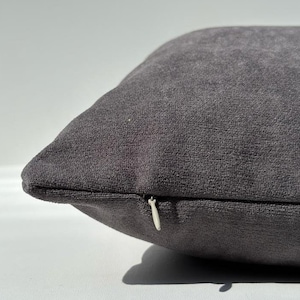 May include: A dark gray throw pillow with a zipper closure. The pillow is made of a soft, textured fabric.