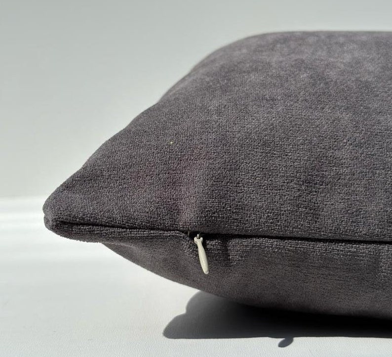 May include: A dark gray throw pillow with a zipper closure. The pillow is made of a soft, textured fabric.