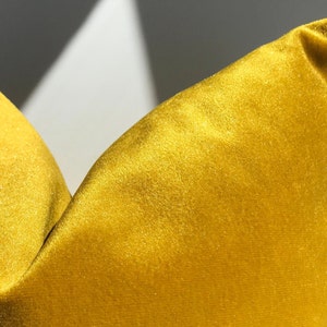 May include: A close-up of a yellow velvet pillow. The pillow is soft and plush, with a subtle sheen.