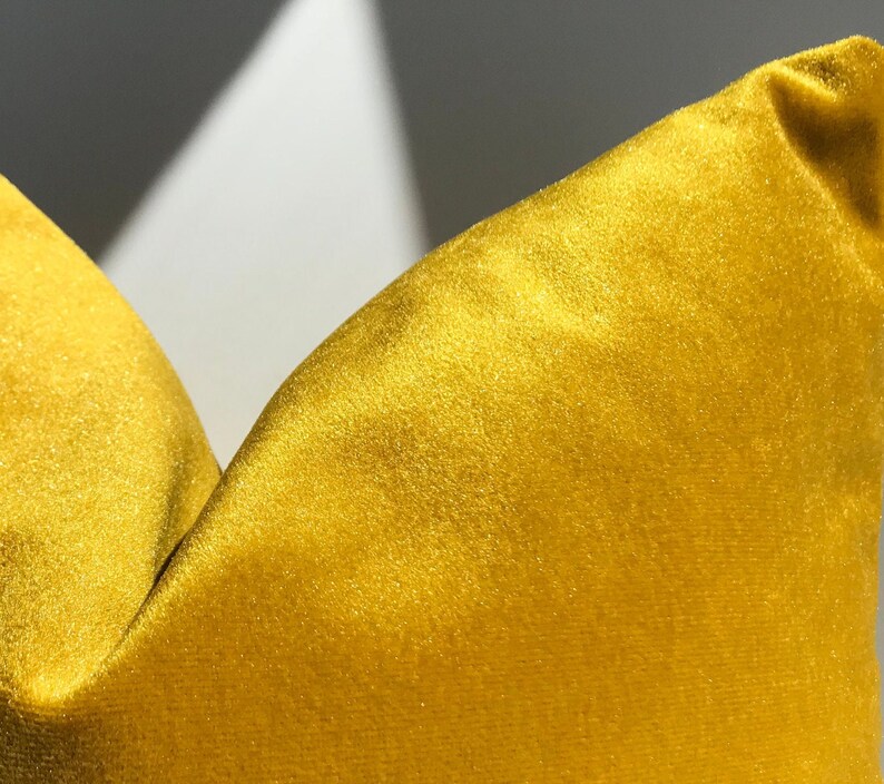 May include: A close-up of a yellow velvet pillow. The pillow is soft and plush, with a subtle sheen.