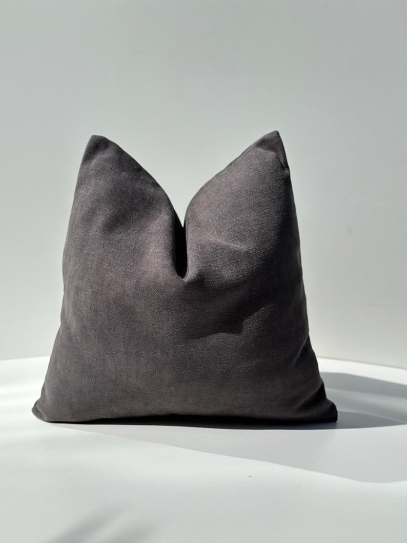 May include: A dark gray throw pillow with a soft, textured fabric. The pillow is square shaped and has a simple design.