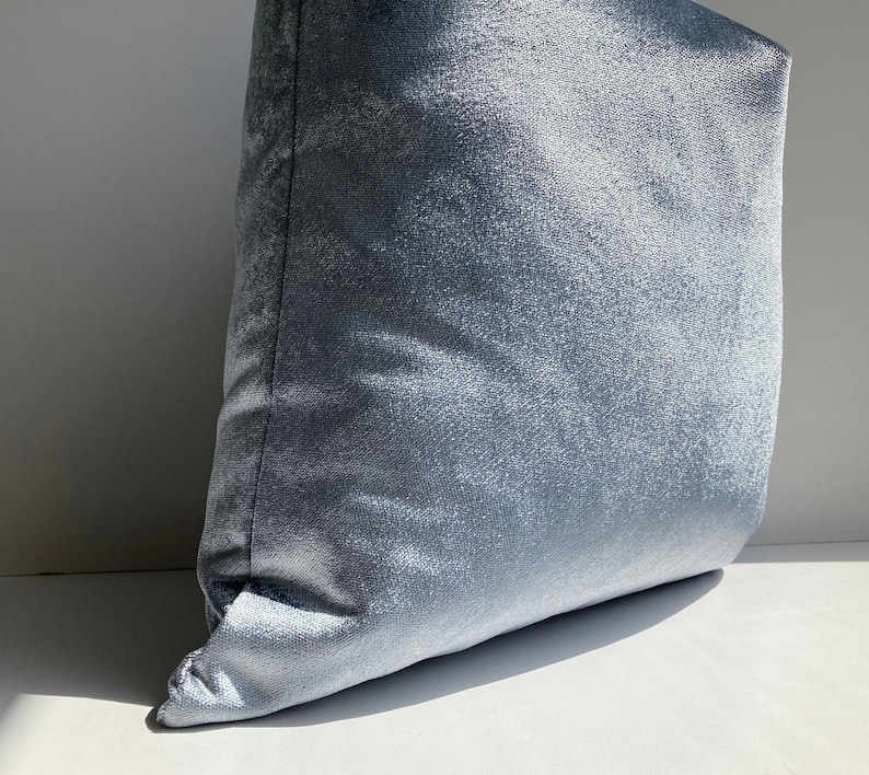 May include: A soft, light blue velvet pillow with a subtle sheen. The pillow is rectangular and has a smooth, plush texture.