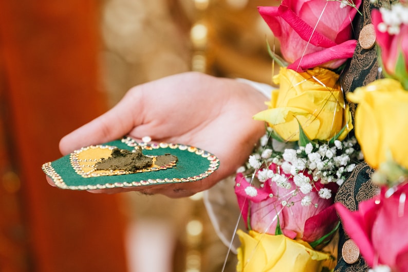 May include: A green heart-shaped tray with gold trim and a small pile of brown paste in the center. The tray is being held in a person's hand.