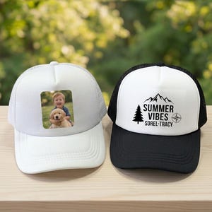 May include: Two trucker caps with mesh backs. The left cap is white and features a rectangular photo print of a child hugging a golden retriever puppy. The right cap has a white front panel with black text reading SUMMER VIBES SOREL-TRACY.