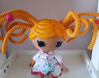 May include: A yellow haired doll with a white dress with red and blue paint splatters. The doll has large black eyes and a pink button nose. The doll's hair is in two long yellow braids.