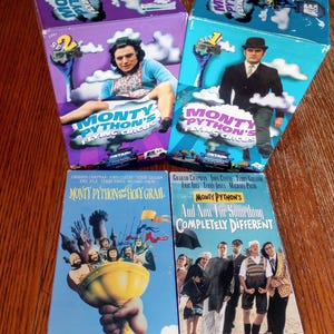 May include: Four vintage Monty Python VHS tapes. Two boxes feature the show's logo and images of the cast. The other two tapes are titled "Monty Python and the Holy Grail" and "And Now For Something Completely Different."