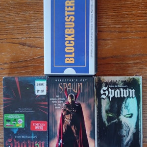May include: Three VHS tapes of the movie Spawn. The first tape is a Blockbuster rental with a blue label. The second tape is a director's cut with a red and black label. The third tape is a Todd McFarlane's Spawn with a black and white label.