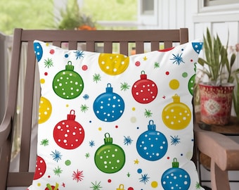 May include: A decorative pillow with a white background featuring a repeating pattern of colorful Christmas ornaments. The ornaments are red, green, blue, and yellow with white polka dots. The pillow is placed on a wooden chair on a porch.