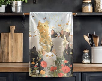 May include: A white kitchen towel featuring a watercolor illustration of several cats in a field of flowers. The cats are various colors, including black, orange, and white, with yellow eyes. Red poppies and other wildflowers are also visible.