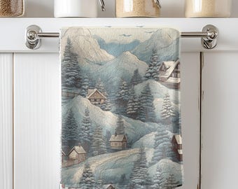 May include: A decorative kitchen towel featuring a winter landscape scene. The design includes snow-covered mountains, evergreen trees, and small cabins. The color palette consists of muted blues, grays, and browns, creating a serene and cozy aesthetic.