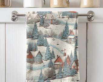 May include: A kitchen towel with a winter village scene. The design features houses with red and blue roofs, snow-covered hills, and evergreen trees. The towel is hanging on a silver bar against a white background.