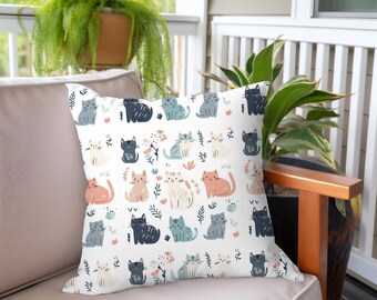 May include: White throw pillow with a repeating pattern of colorful cartoon cats on a white background. The cats are in various poses and colors, including pink, blue, and gray.