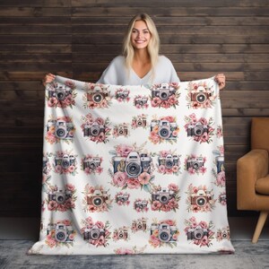 May include: White fleece blanket with a repeating pattern of vintage cameras and pink flowers.