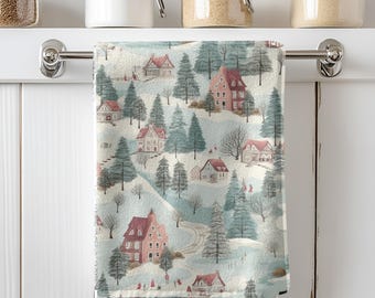 May include: A decorative kitchen towel featuring a winter village scene. The design includes houses with red roofs, evergreen trees, and a snowy landscape. The towel is hanging on a silver bar against a white background.