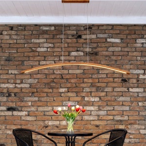 Könnte beinhalten: Eine gebogene Holzpendelleuchte mit warmweißem Licht hängt über einem Tisch mit zwei schwarzen Stühlen. Eine Vase mit roten, weißen und rosa Tulpen steht auf dem Tisch.