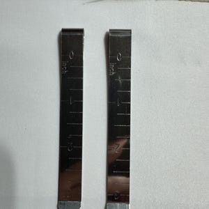 May include: Two silver measuring tapes with inch markings, each measuring up to 3 inches.