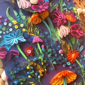 May include: A dark blue fabric pouch with a colorful floral design. The flowers are made of paper and are in shades of pink, orange, yellow, blue, and green. The pouch has a flap with a snap closure.