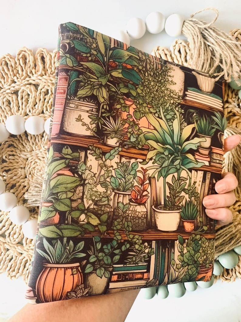 May include: A brown fabric pouch with a colorful print of potted plants and books on a shelf. The print features a variety of green plants in different pots, with some books visible on the shelves.