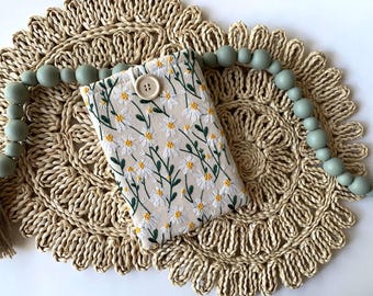 May include: A rectangular fabric pouch featuring an embroidered pattern of white daisies with yellow centers and green stems on a beige background, secured with a single beige button closure at the top center.