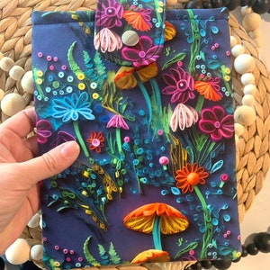 May include: A blue fabric pouch with a colorful floral pattern featuring flowers, leaves, and mushrooms. The pouch has a flap with a button closure.
