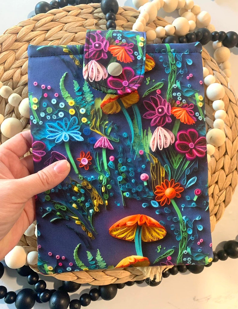 May include: A blue fabric pouch with a colorful floral pattern featuring flowers, leaves, and mushrooms. The pouch has a flap with a button closure.