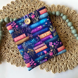 May include: A dark blue book cover with a pattern of colorful books and flowers. The cover has a button closure and a purple ribbon.
