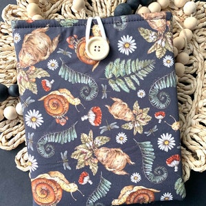May include: A black fabric book cover with a repeating pattern of snails, mushrooms, ferns, and flowers. The cover has a white button closure.