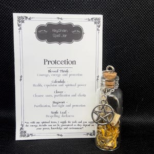 May include: A small glass bottle charm with a silver pentagram charm and a cork stopper. The bottle contains dried herbs and is labeled "Protection" with a list of herbs and their properties: Blessed Thistle, Calendula, Clover, Mugwort, and Nettle Leaf. The label also includes the text "Keychain Spell Jar" and "As with any spiritual items, I supply the tools and you supply the energy. Results can not be guaranteed as they depend on your power, knowledge and environment."