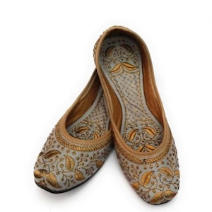 K&ouml;nnte beinhalten: Ein Paar graue flache Schuhe mit goldenen Stickereien und floralen Mustern. Die Schuhe haben eine spitze Zehenpartie und einen niedrigen Absatz.