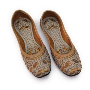 K&ouml;nnte beinhalten: Ein Paar graue, bestickte flache Schuhe mit goldenen Blumendesigns. Die Schuhe haben eine spitze Zehenpartie und eine flache Sohle.