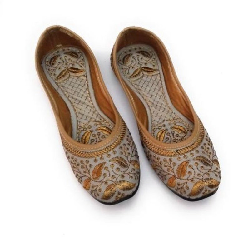 K&ouml;nnte beinhalten: Ein Paar graue, bestickte flache Schuhe mit goldenen Blumendesigns. Die Schuhe haben eine spitze Zehenpartie und eine flache Sohle.