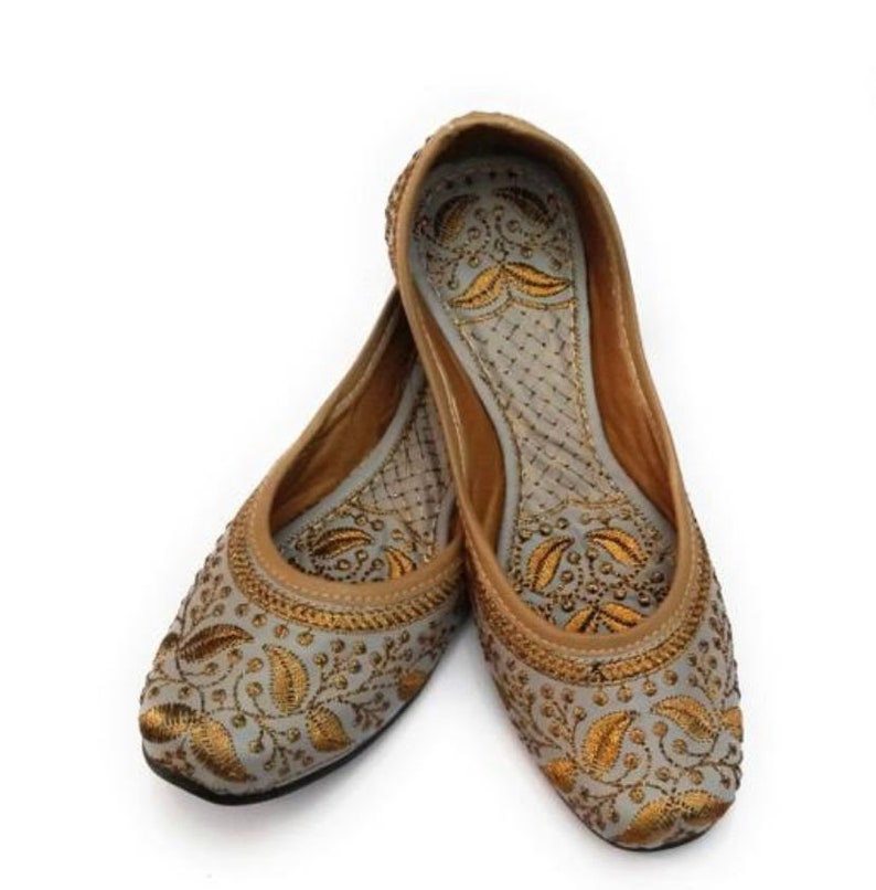 K&ouml;nnte beinhalten: Ein Paar graue, bestickte flache Schuhe mit goldenen Blumendesigns. Die Schuhe haben eine spitze Zehenpartie und eine flache Sohle.