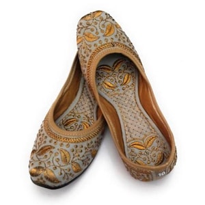 K&ouml;nnte beinhalten: Ein Paar graue flache Schuhe mit goldenen Stickereien und floralen Mustern. Die Schuhe haben eine spitze Zehenpartie und eine flache Sohle.