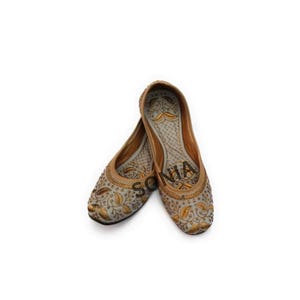 K&ouml;nnte beinhalten: Ein Paar graue, bestickte flache Schuhe mit goldenen Details. Die Schuhe haben eine spitze Zehenpartie und eine flache Sohle.