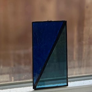 May include: A small stained glass window with a diagonal design. The top half is a dark blue color and the bottom half is a light blue color.