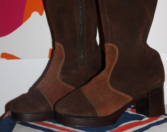May include: A pair of brown suede knee-high boots with a chunky heel. The boots have a zipper on the inside of each leg and a contrasting brown suede panel on the front.
