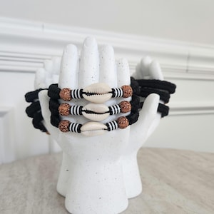 May include: Three black cord bracelets with white and brown beads and white seashells.