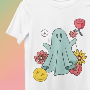 May include: A white t-shirt with a blue ghost wearing a peace sign, a yellow smiley face, and pink, red, and yellow flowers printed on it.