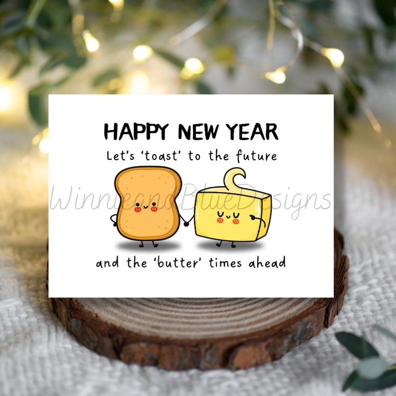 May include: A white card with a happy new year greeting. The card features a cartoon illustration of a slice of bread and a stick of butter holding hands. The text reads "Happy New Year. Let's 'toast' to the future and the 'butter' times ahead."