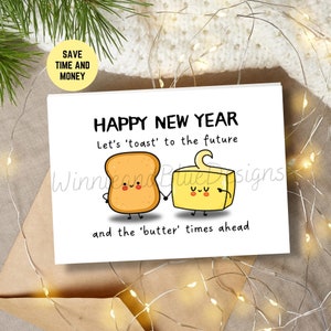 May include: A white card with a happy new year greeting. The card features a cartoon illustration of a slice of toast and a stick of butter holding hands. The text reads "Happy New Year. Let's 'toast' to the future and the 'butter' times ahead."