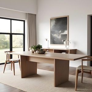 May include: A light wood dining table with a rectangular top and two thick, rectangular legs. The table is set in a modern dining room with a large window and a beige rug.