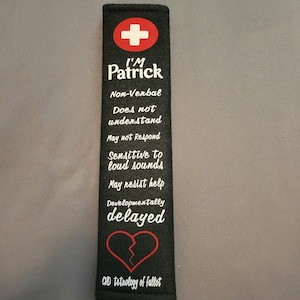 May include: Black fabric car seat belt cover with a red cross, the text "I'M Patrick", and the words "Non-Verbal, Does not understand, May not Respond, Sensitive to loud sounds, May resist help, Developmentally delayed, CHD tetrology of fallot".
