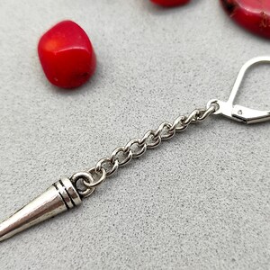 May include: Silver earring with a pointed, cone-shaped charm and a chain link. The earring has a hook closure.
