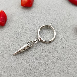 May include: Silver hoop earring with a bullet charm hanging from it.