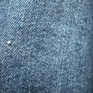 May include: Close-up of a blue denim fabric with a diagonal weave pattern.
