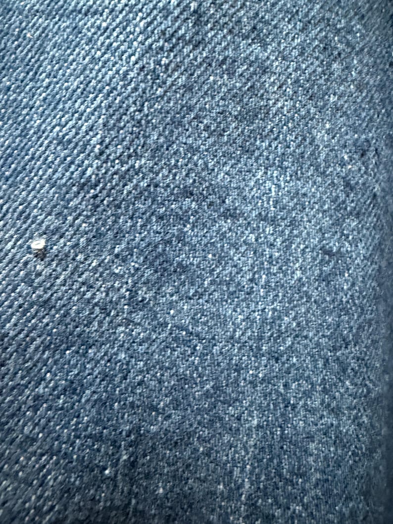 May include: Close-up of a blue denim fabric with a diagonal weave pattern.