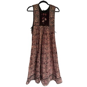 Könnte beinhalten: Ein ärmelloses, bodenlanges Kleid mit einem Blumenmuster in Rosa-, Braun- und Schwarztönen. Das Kleid hängt an einem schwarzen Kleiderbügel. Das Oberteil hat eine dunklere braune Blende mit floralen Stickereien.