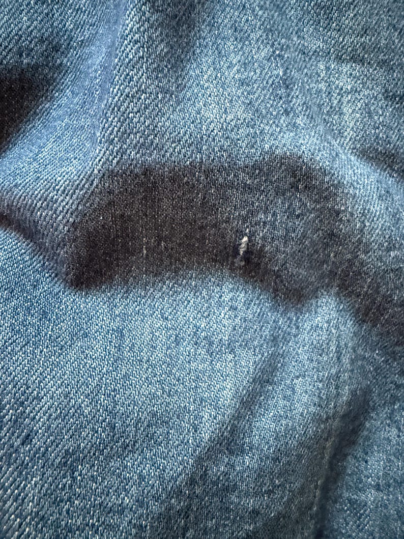May include: Close-up of a blue denim fabric with a textured weave. The fabric is folded and wrinkled, showing the natural texture of the material.